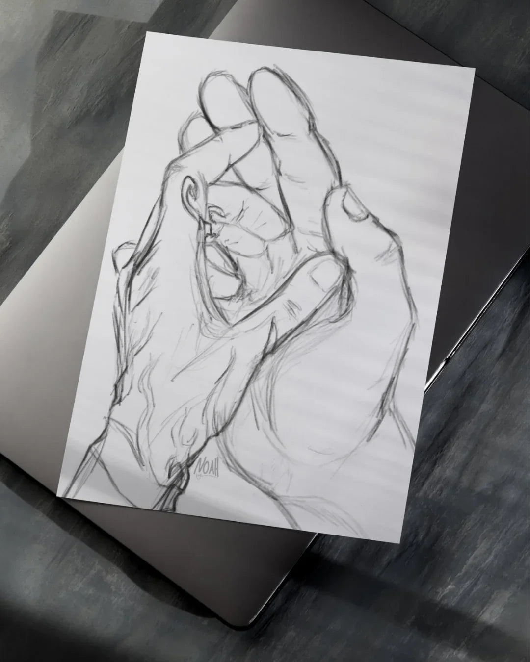 Black and white pencil sketch of two hands holding a ring, placed on a laptop on a dark surface