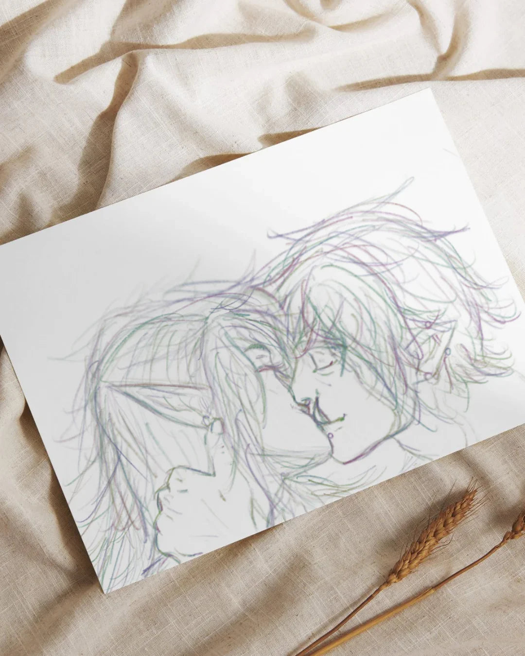 Hand-drawn sketch of two elf characters intimately touching foreheads on white paper over beige fabric