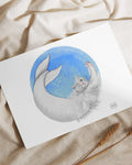 Illustration of a gray cat with a mermaid tail curling in a blue circular background on white paper