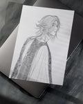 Black and white pencil sketch of a person with long hair and cloak on white paper, placed on laptop keyboard
