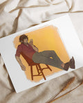 Art print of man with brown hair in red shirt and gray pants reclining on wooden chair with orange background