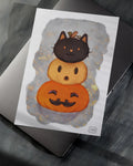 Halloween illustration of stacked pumpkins with a black cat head on top on a paper over laptop
