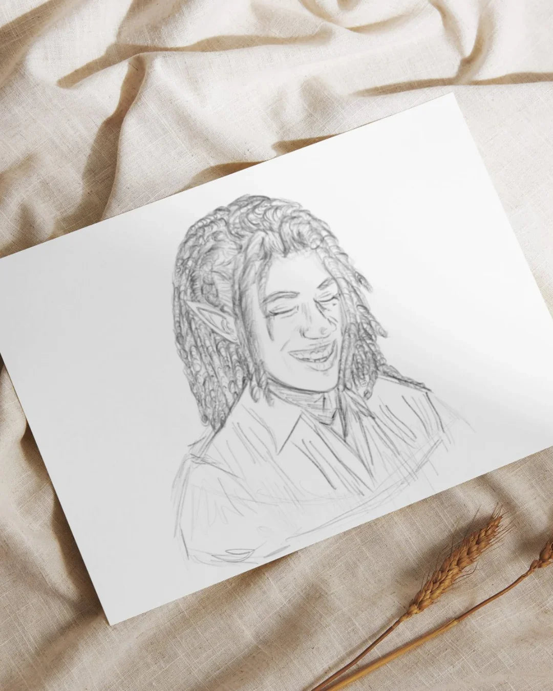 Pencil sketch of a smiling elf with dreadlocks and pointed ears on white paper, lying on beige fabric